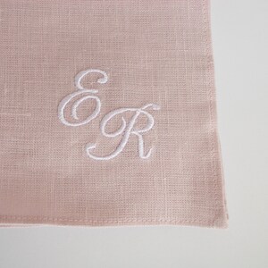 May include: A pale pink linen napkin with white embroidered initials "E & R" in a cursive font.