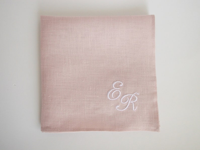 May include: A pale pink linen handkerchief with white embroidered initials "E & R" in a cursive script.