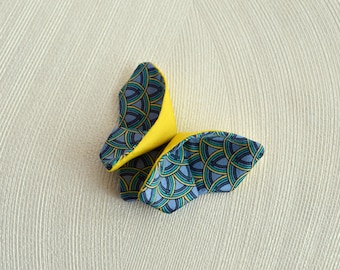 May include: A decorative butterfly-shaped object with yellow wings and patterned blue fabric. The fabric features a repeating design of curved lines in shades of blue and yellow. The object is likely a decorative item or accessory.