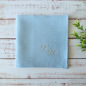 Puede incluir: Un pañuelo de lino azul claro con las iniciales bordadas "L.M."