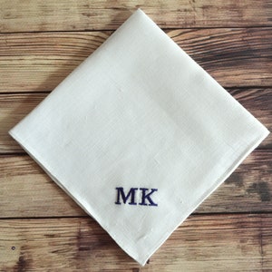 Peut inclure: Un mouchoir de poche en lin blanc avec les initiales "MK" brodées en fil bleu.