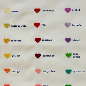 May include: A white fabric sample featuring embroidered heart shapes in various colors. Colors include white, cream, antique gold, mustard, yellow, orange, salmon, copper, terracotta, red, marsala, burgundy, baby pink, pink, mauve, orchid, lavender, violet, lime green, aquamarine, and lawn green.
