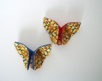 May include: Two origami butterflies made from fabric. The butterflies are folded in a traditional style and have a yellow and blue pattern with red accents.