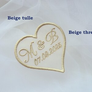 May include: A heart-shaped embroidered patch with the initials "M & B" and the date "07.09.2025" in beige thread. The patch is set against a backdrop of white tulle fabric, creating a delicate and romantic aesthetic, suitable for weddings.