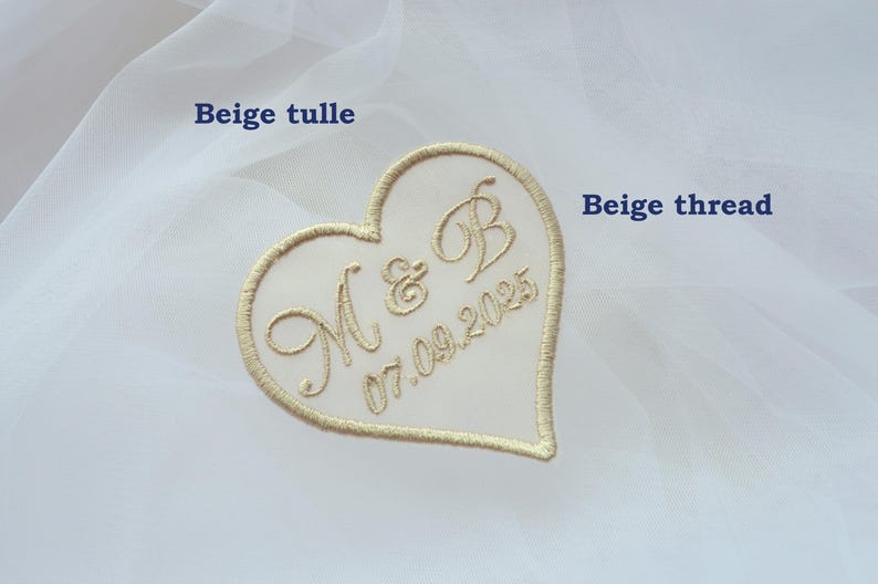 May include: A heart-shaped embroidered patch with the initials "M & B" and the date "07.09.2025" in beige thread. The patch is set against a backdrop of white tulle fabric, creating a delicate and romantic aesthetic, suitable for weddings.