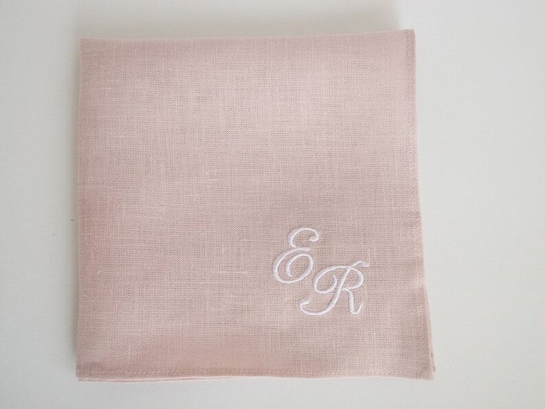 May include: A pale pink linen handkerchief with white embroidered initials "E & R" in a cursive script.