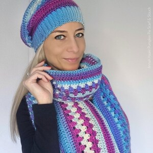 Op de afbeelding: Een gehaakte muts en sjaal set in blauwe, paarse en roze tinten. De muts is een slouch stijl, en de sjaal heeft een granny stitch patroon. De tekst "Annah Haakt Pumpkin Pie Scarf & Slouch" is zichtbaar.