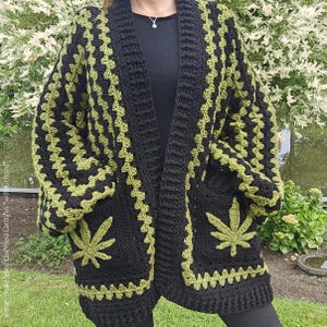 May include: A black and green crocheted cardigan with a leaf design. The cardigan has pockets on the front and a long, open front.
