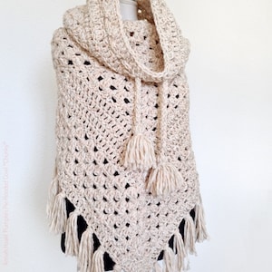 Op de afbeelding: Een chunky, crèmekleurige gehaakte capuchon met een gestructureerd steekpatroon. De cowl heeft een capuchon, kwastjes en franjes langs de onderrand. Het ontwerp is handgemaakt en geschikt voor koud weer.