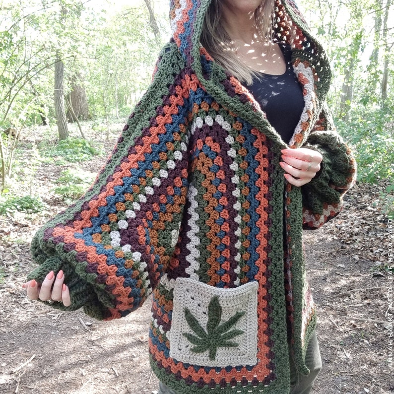May include: A green, brown, orange, and blue crocheted cardigan with a hood and a large marijuana leaf pocket. The cardigan is worn by a person in a forest setting.