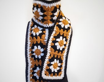 May include: A crocheted scarf with a black, white, and mustard yellow color pattern. The scarf is made with granny squares and has a cowl neck.