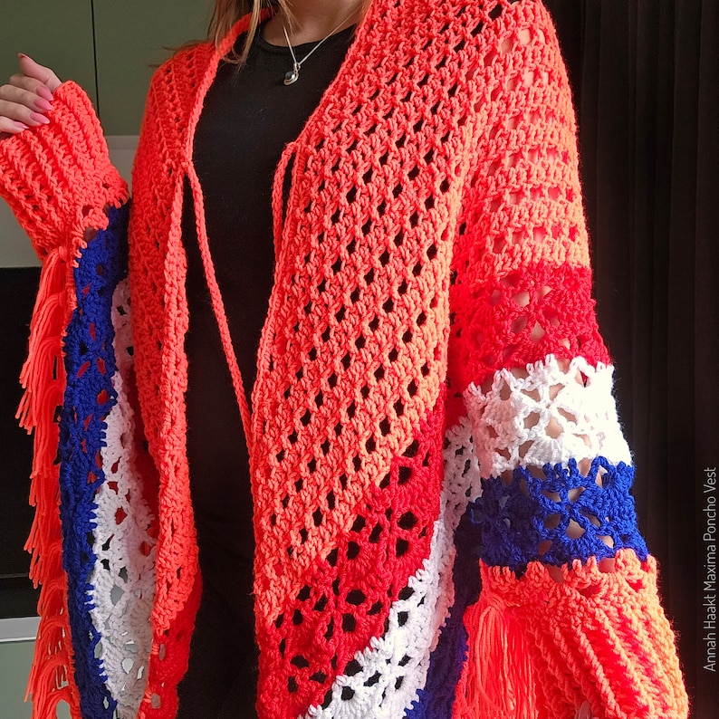 Puede incluir: Un chaleco poncho de ganchillo con un patr&oacute;n de rayas de colores en rojo, blanco y azul. El chaleco tiene un dobladillo con flecos y un cierre de corbata en el cuello. El chaleco est&aacute; hecho con un hilo ligero y tiene un ajuste holgado y fluido.