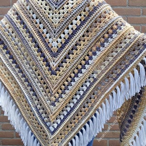 Op de afbeelding: Een handgemaakte gehaakte sjaal in een geometrisch patroon. De sjaal heeft een kleurenpalet van beige, crème en marineblauw. Witte franjes sieren de randen. De tekst "Annah Haakt Cozy Shawl" is zichtbaar.