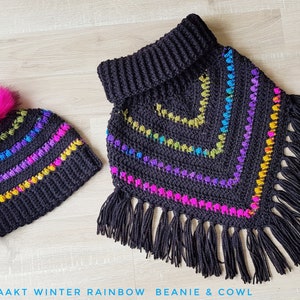Op de afbeelding: Een zwarte gehaakte beanie met een roze pompon en een bijpassende zwarte gehaakte cowl met regenboogstrepen en franjes. De beanie en cowl zijn handgemaakt en hebben een uniek winterregenboogontwerp.