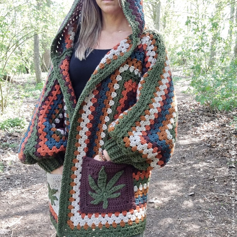 May include: A crocheted cardigan with a hood, featuring a colorful striped pattern and a large green leaf design on the pocket. The cardigan is made with a variety of colors, including green, brown, orange, and blue.