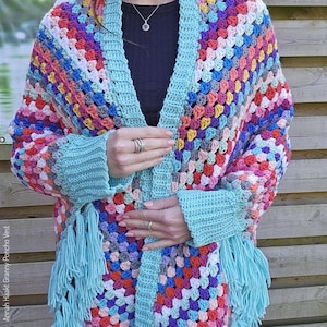 Op de afbeelding: Een kleurrijk gehaakt poncho-vest met een granny square-patroon en franjes. Het vest is open aan de voorkant en heeft een lichtblauwe kleur.