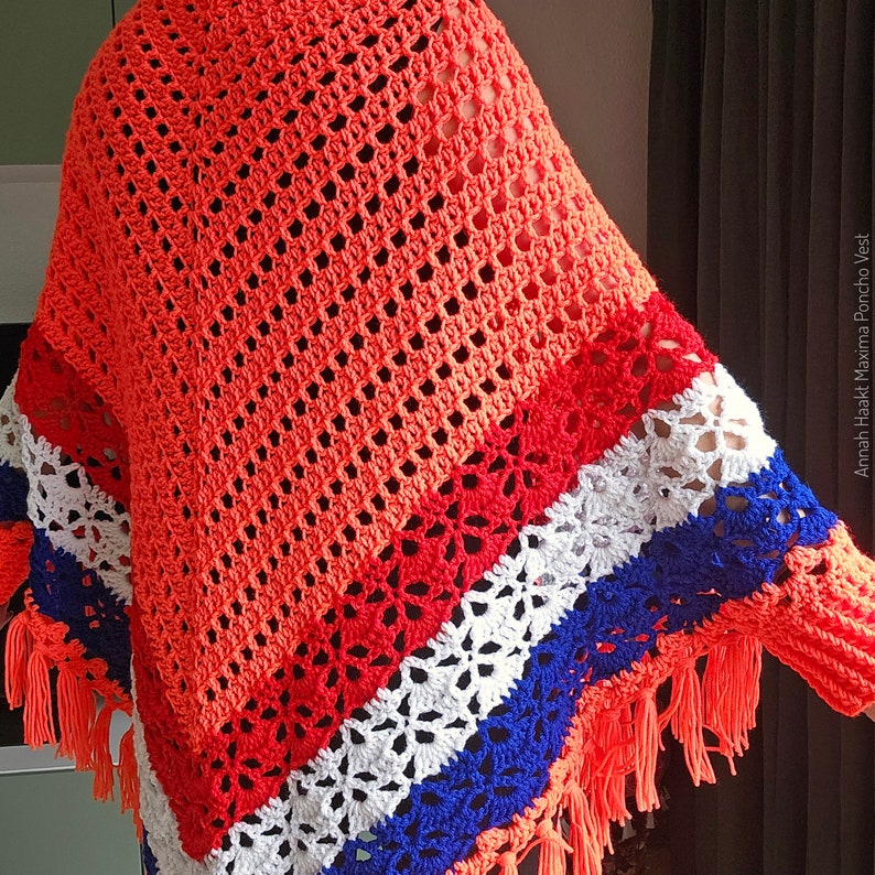 Puede incluir: Un chaleco poncho de ganchillo con un patr&oacute;n de rayas de colores en tonos naranja, rojo, blanco y azul. El chaleco tiene una forma triangular y flecos en los bordes.