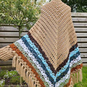 Puede incluir: Un poncho de ganchillo con un patr&oacute;n de rayas marrones, blancas, azules, verdes y naranjas. El poncho tiene un borde de flecos y est&aacute; hecho con un punto de encaje.