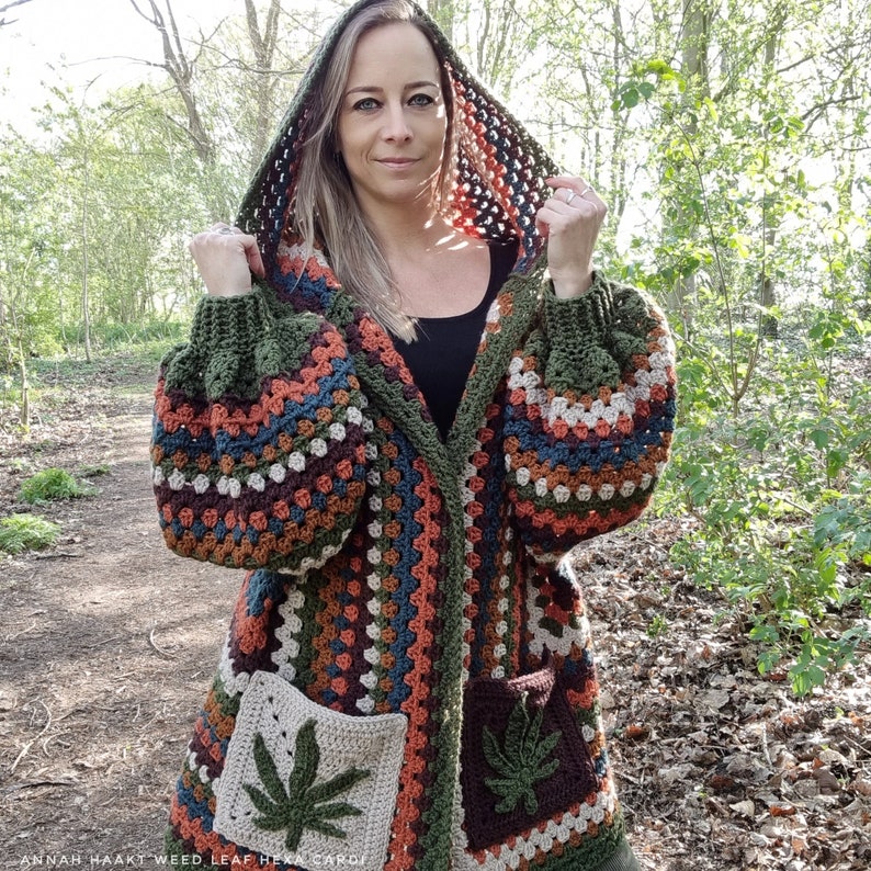 May include: A hooded cardigan with a colorful crocheted pattern featuring a leaf design. The cardigan has pockets with a leaf design and a hood.