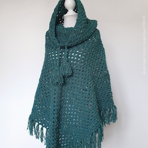 Könnte beinhalten: Ein türkisfarbener Häkel-Kapuzenponcho mit einem Quastenband. Der Poncho ist mit einem Granny-Stichmuster gearbeitet und hat Fransenbesatz.