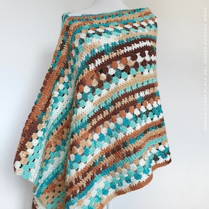 Op de afbeelding: Een gehaakt poncho met een diagonaal patroon in tinten bruin, turquoise, wit en crème. De poncho is gemaakt met een granny square steek.