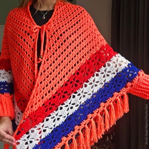 Puede incluir: Un poncho de ganchillo con un patr&oacute;n de rayas de colores en rojo, blanco y azul. El poncho tiene un cierre de corbata y un borde de flecos.