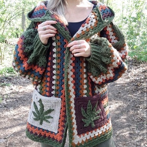 May include: A green, brown, and beige crocheted cardigan with a hood and two large pockets featuring a marijuana leaf design.