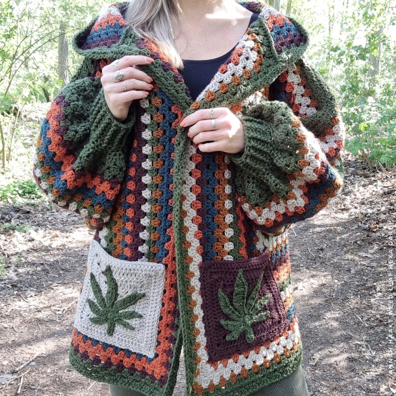 May include: A green, brown, and beige crocheted cardigan with a hood and two large pockets featuring a marijuana leaf design.