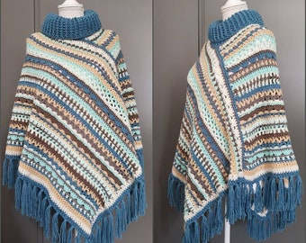 May include: A crocheted poncho with a striped pattern in shades of blue, brown, beige, and white. The poncho has a high neck and a fringe trim. The poncho is displayed on a mannequin.