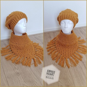 May include: A crocheted mustard yellow beanie and matching cowl with fringe. The beanie and cowl are displayed on a white mannequin head against a wood background. The text "ANNAH HAAKT GRANNY MUTS & COL" is visible in the bottom right corner of the image.