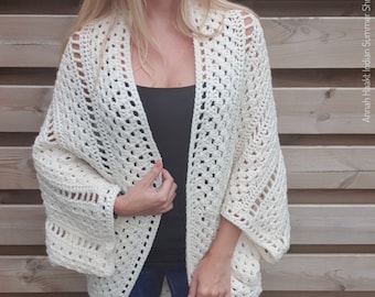 May include: A white crochet shrug with a loose, open weave. The shrug has a long, flowing silhouette and is perfect for layering over a tank top or t-shirt.