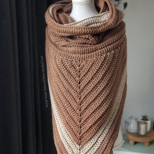 Könnte beinhalten: Ein brauner und beiger Häkelkragen mit Kapuze. Der Kragen hat eine dreieckige Form mit einem strukturierten Stichmuster. Die Kapuze ist umgeschlagen und hat ein beiges Futter. Der Text "Annah Haakt Textured Boho Hooded Cowl" ist sichtbar.