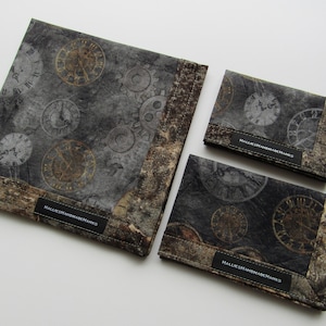 Könnte beinhalten: Drei graue Stoffbeutel mit einem sich wiederholenden Muster aus Uhren und Zahnrädern. Die Beutel haben einen braunen Rand und ein schwarzes Etikett mit der Aufschrift "Hallelujah Handmade".
