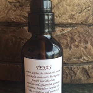 May include: A brown glass bottle with a black pump top and a white label that reads "TEJAS" and lists ingredients including "jojoba, hazelnut oil, neem, vita kola, shatavari, bergamot, fennel, rose absolute, sandalwood, spearmint, jasmine absolute, lavender essential oil (the revitalizer and source of pure dosha)"