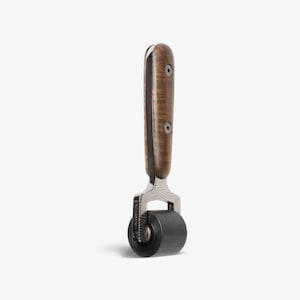 May include: A small, black rubber roller with a silver metal frame and a wooden handle. The handle has a wood grain pattern and two silver screws.