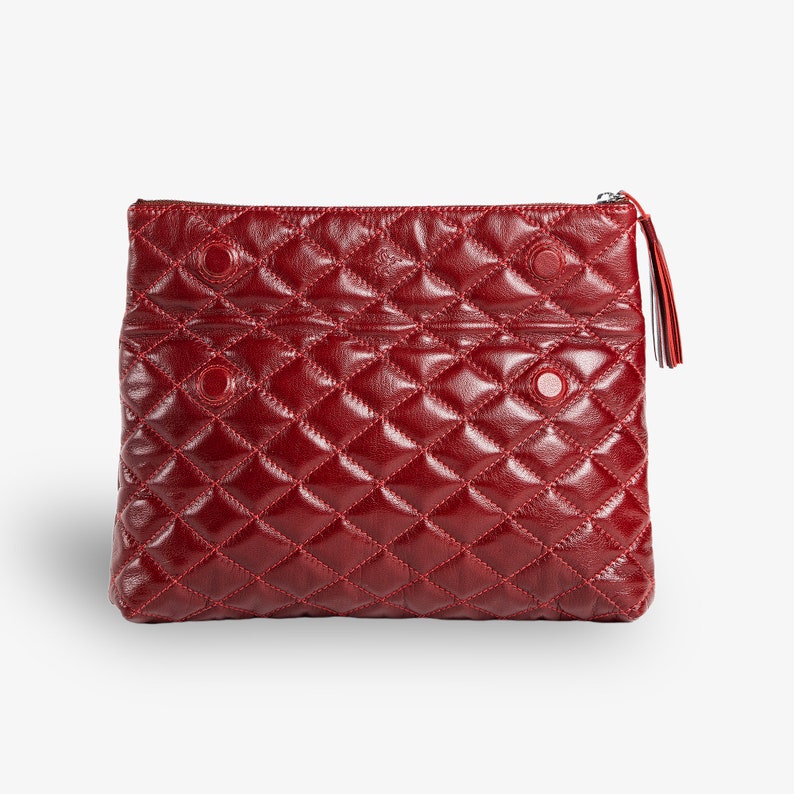 Op de afbeelding: Een gestikte clutch van bordeauxrood leer met een ritssluiting en een kwast.
