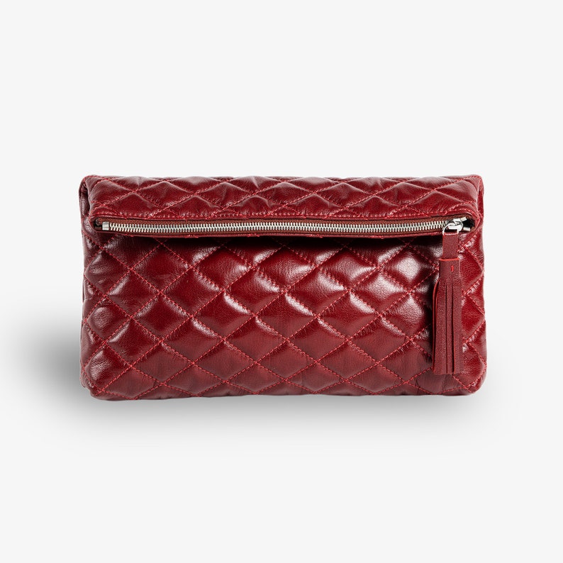 Op de afbeelding: Een bordeauxrode quilted leren clutch met een zilveren rits en een kwast.