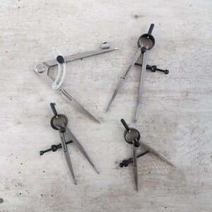 Könnte beinhalten: Vier silberne Zirkel mit schwarzen Akzenten. Die Zirkel befinden sich auf einer hellgrauen, strukturierten Oberfläche. Die Zirkel sind mit "TANNENSTEIN" beschriftet.