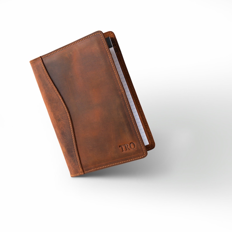 May include: A brown leather notebook with a pen holder and the initials "TRO" embossed on the front.