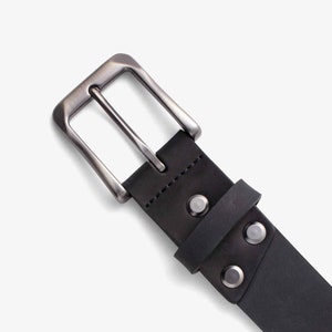 May include: A black leather belt with a silver buckle and metal rivets. The belt is made of a durable material and has a classic design.