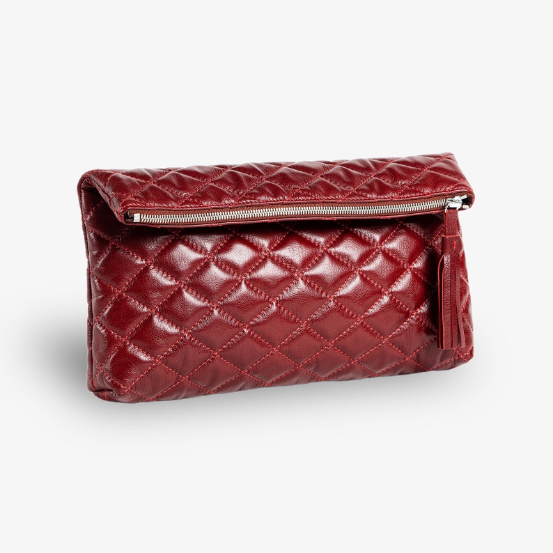 Op de afbeelding: Een bordeauxrode quilted leren clutch met een ritssluiting en een kwast.