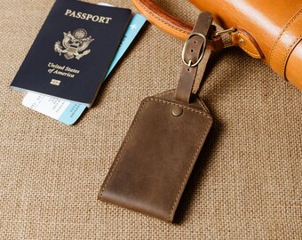 Op de afbeelding: Een bruine leren bagagelabel met een messing gesp en een paspoort met de woorden "United States of America" op de omslag.