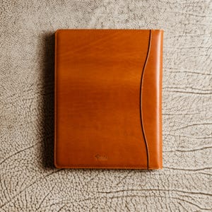 May include: A brown leather portfolio with a curved edge and the word "Ferrari" embossed on the front.