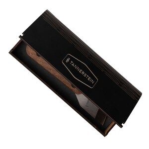 Op de afbeelding: Een zwarte houten doos met een gouden logo met de tekst "TANNERS TEIN" en een houten en metalen gereedschap erin.