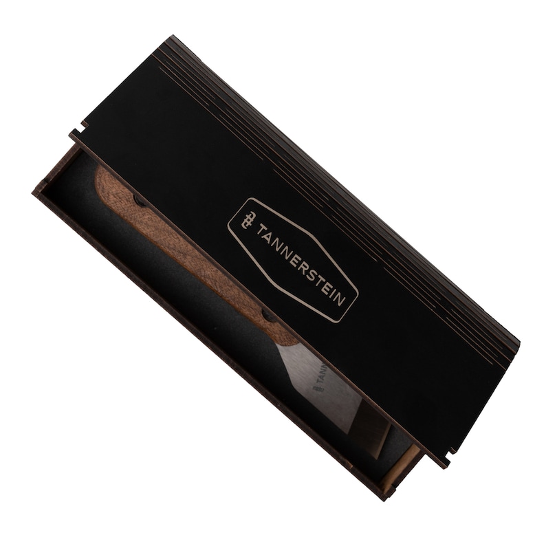 Op de afbeelding: Een zwarte houten doos met een gouden logo met de tekst "TANNERS TEIN" en een houten en metalen gereedschap erin.