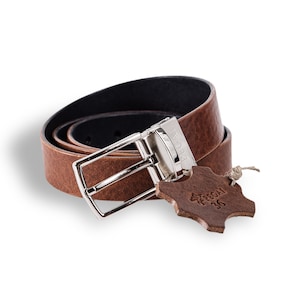 May include: A brown leather belt with a silver buckle. The belt is reversible and has a black leather side. The buckle has the word "PEGASI" engraved on it. The belt is accompanied by a brown leather tag with the word "PEGASI" and the number "36" printed on it.