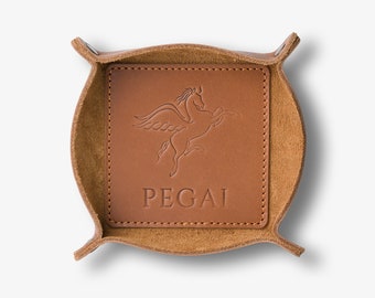 May include: A brown leather catchall tray with a winged horse design and the word "PEGAI" embossed on the front.
