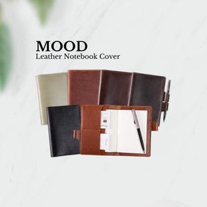 May include: A set of leather notebook covers in various colors, including black, brown, and green. The covers are made of a textured leather and have a pen holder and card slots. The text "MOOD Leather Notebook Cover" is displayed above the covers.