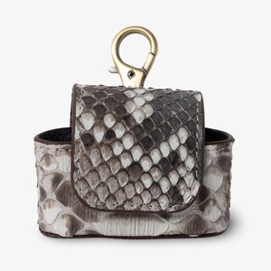 May include: A small, white and brown snakeskin leather case with a gold-toned metal hook. The case has a flap that closes with a snap.