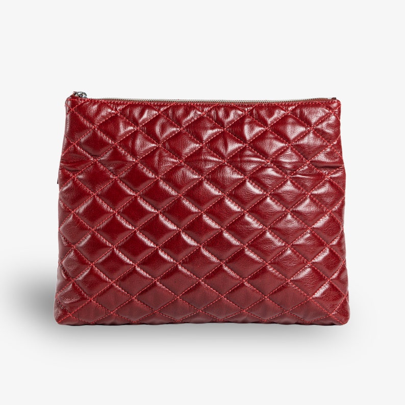 Op de afbeelding: Een gestikte clutch van bordeauxrood leer met een ritssluiting.